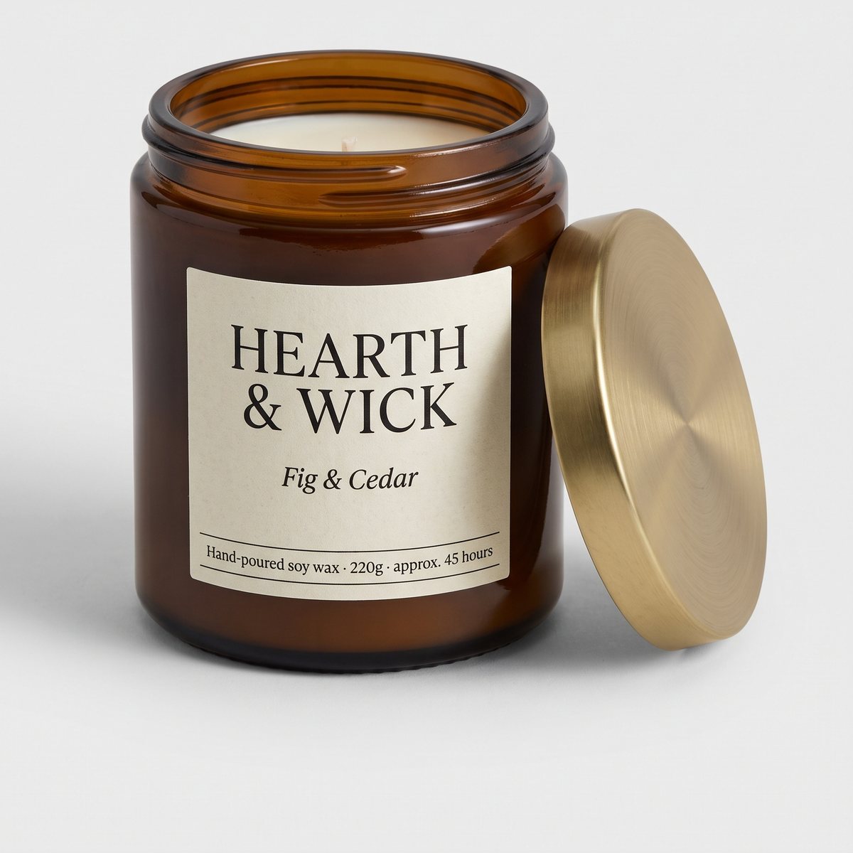 The original photo: a scented candle in an amber glass jar with a cream label reading HEARTH & WICK, Fig & Cedar, and a brushed brass lid leaning beside it, on a plain light grey background