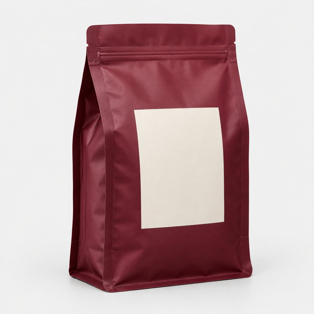A burgundy resealable coffee pouch with a blank cream label on a plain background