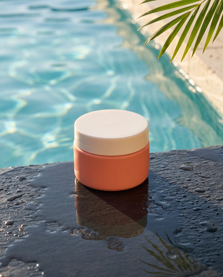 The coral cream jar on wet stone beside a pool in bright sunlight